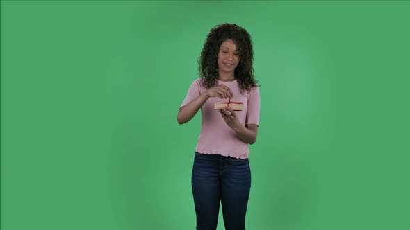 Portrait of Beautiful African American Young Woman Is Looking at Camera and Opening the Gift with a