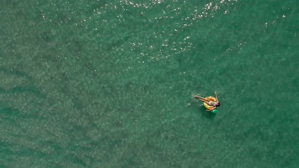 Aerial Top View of Turquoise Sea Water and Woman Swimming on the Yellow Swim Ring