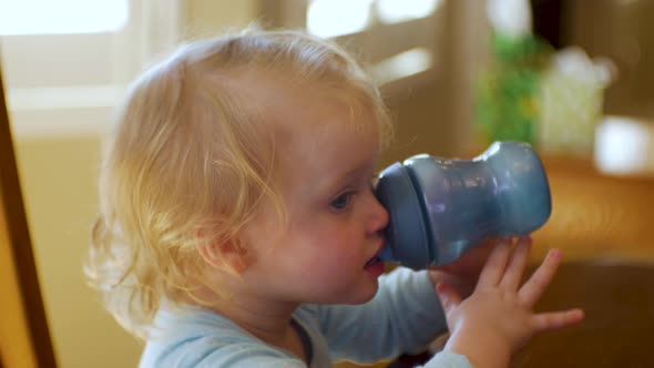 Adorable female toddler drinks water, joice or milk from her sippy cup - close up