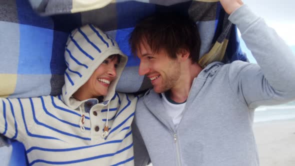 Happy couple hiding in blanket at beach