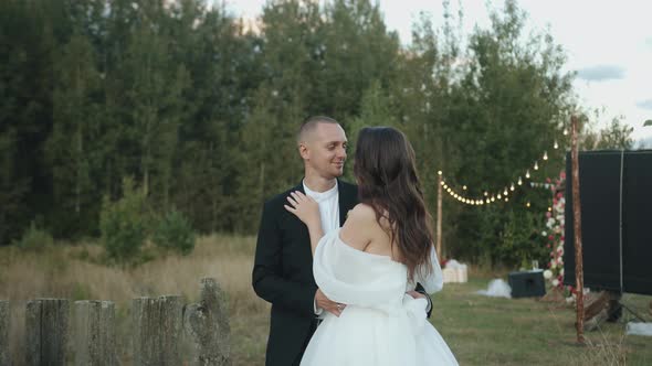 The Groom Hugs the Bride and Kisses Her on the Cheek at the Decorated Outdoor Wedding Venue