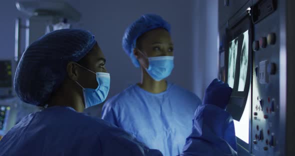 Mixed race female surgeons wearing protective clothing looking at x-ray on screen