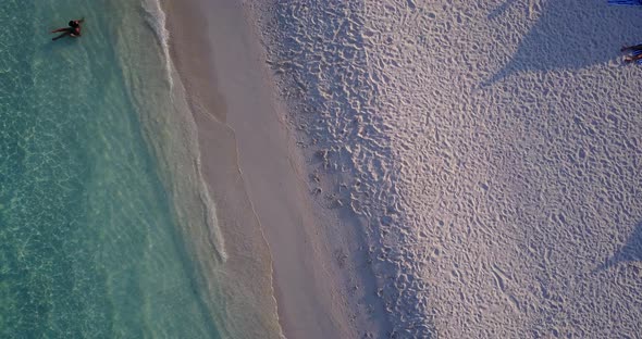 Wide overhead tourism shot of a sunshine white sandy paradise beach and blue ocean background in 4K