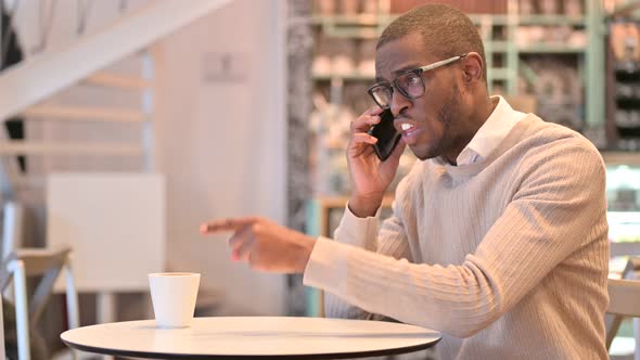 Upset African Man Angry on Smartphone in Cafe 