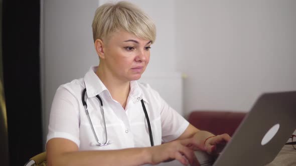 The Concentrated Adult Woman Doc is Filling the Symptoms Into Laptop