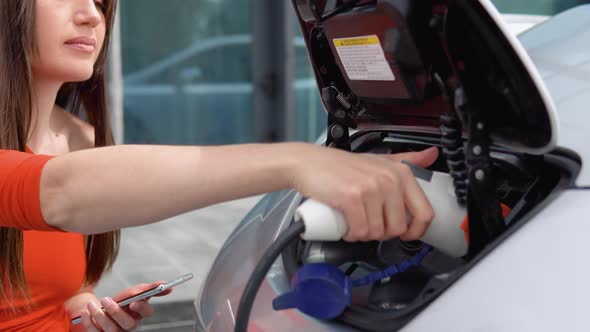 Woman Puts Charger Into Her Electric Car and Use Phone When Waiting