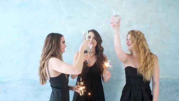 Sexy girls clink glasses with champagne. Women dance sparklers in hands