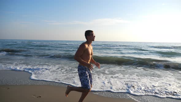 Athletic Handsome Guy Jogging Through Coast with Beautiful Seascape at Background. Young Sporty Man