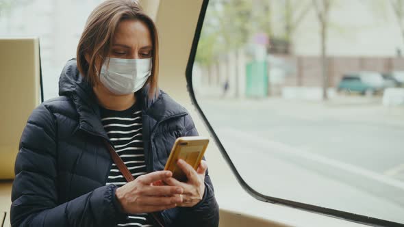 A Young Adult Woman Wearing a Facial Mask Uses a Smartphone While Riding a Bus