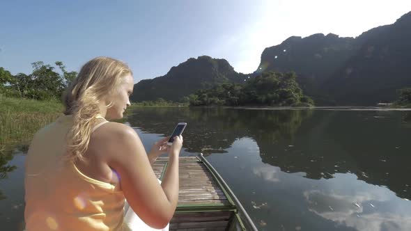 Woman traveler with mobile taking shots during Trang An boat tour, Vietnam