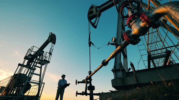 Engineer with Laptop Controls Oil Extraction Between Two Oil Pumpjacks