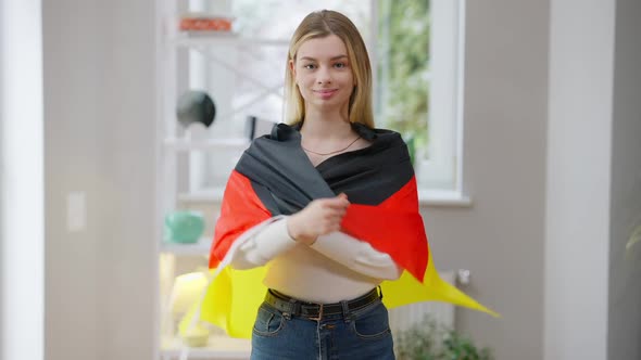 Portrait of Confident Young Woman Wrapping in German Flag Looking at Camera Smiling