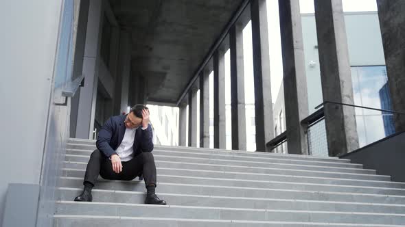 young asian depressed man sitting on the stairs outdoors street near office business 