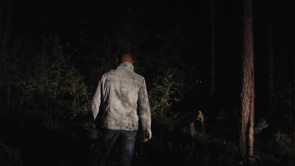 A Man Stands with His Back Turned at Night in the Forest Looking Around