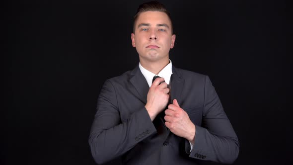 Young Businessman Straightens His Suit. Man in a Black Suit on a Black Background