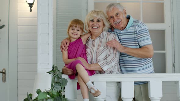 Senior Grandfather and Grandmother Couple with Granddaughter Waving Hand, Smiling, Saying Hello