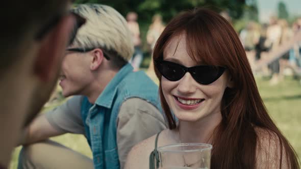 Close up of caucasian ginger hair woman drinking beer from disposable cup at music festival and chat