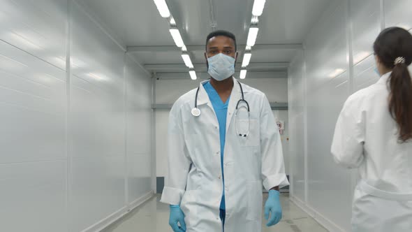 African Doctor in Safety Mask and Gloves Walking in Hospital Corridor