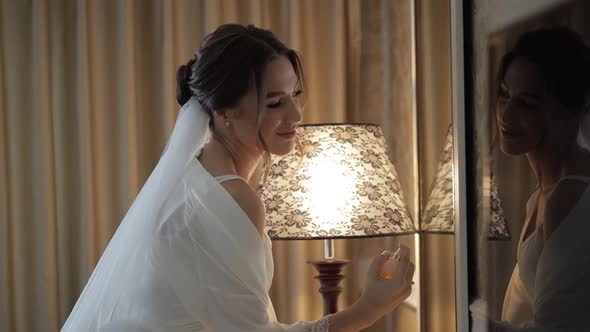 Bride in White Boudoir Dress Stay Near Mirror Looking at Reflection Using Perfume or Deodorant