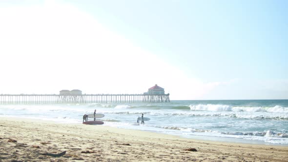 A family goes surfing at the beach during a hazy sunrise with the Huntington Beach Pier in the backg