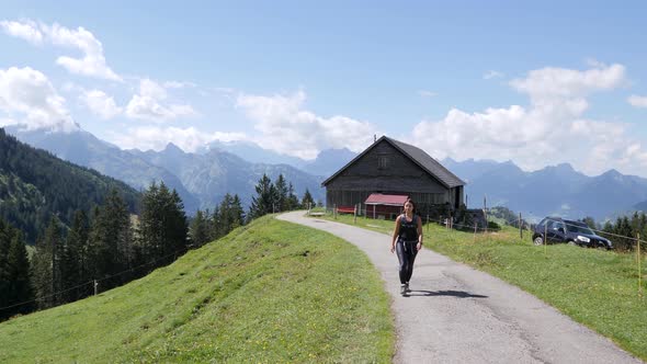 Pretty woman hiking on rural path during sunny day with beautiful alp mountains in background.Amden,