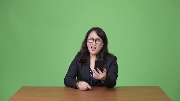 Mature Beautiful Asian Businesswoman Using Phone and Getting Bad News