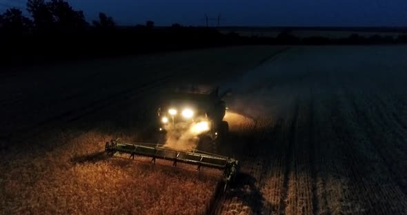 Combine harvester working on a wheat crop at night. Aerial view.