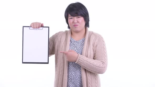 Stressed Overweight Asian Woman Showing Clipboard and Giving Thumbs Down Ready for Winter