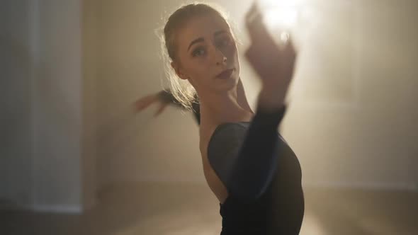 Slender Beautiful Ballerina Spinning Fast in Backlit Spotlight Looking at Camera