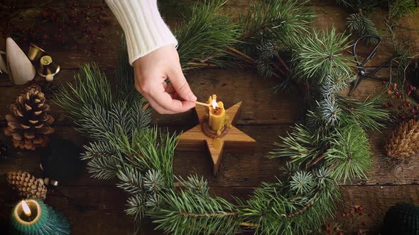 Hand in sweater lighting up candle in christmas wreath on rustic wooden table