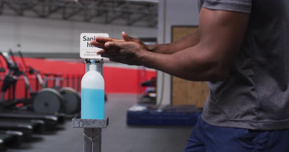 Mid section of fit african american man sanitizing his hands in the gym