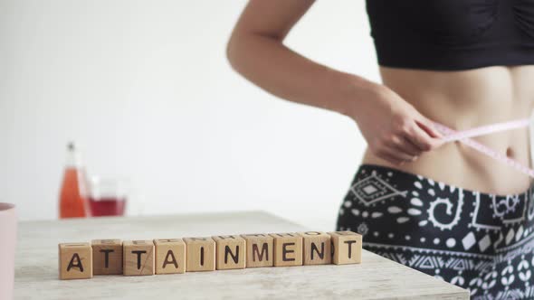 Expression Attainment Is Made Up Of Cubes. Young Woman Measures Her Waist With A Measuring Tape