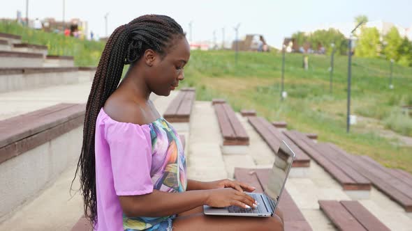 African-American Woman Works on Modern Laptop on Bench
