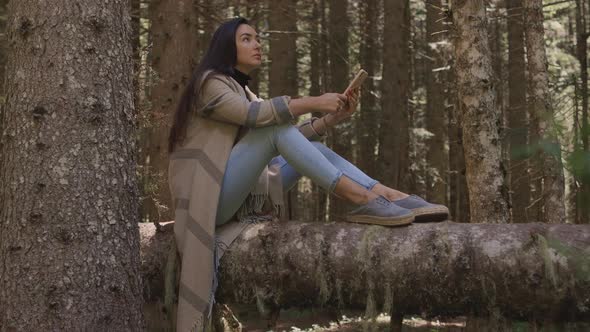 Pretty Woman Using Phone in Forest Sitting on Wooden Log