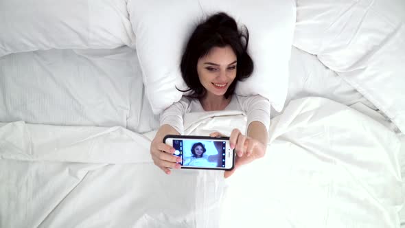 Beautiful Woman Making Photo On Mobile Phone In Bed