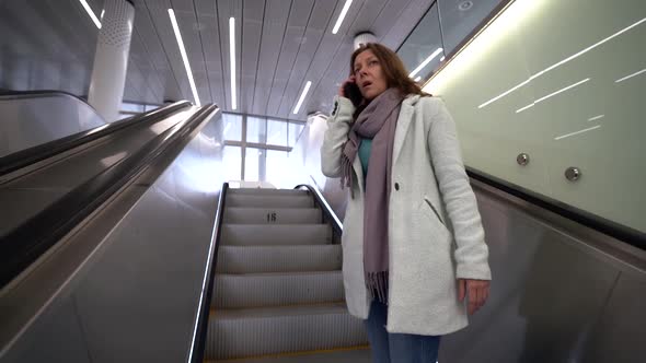 Sad Woman Rides Up the Escalator in the Subway, She Is in a Public Place, Talking on the Phone. She