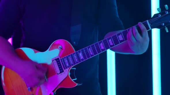 A Musician Plays a Solo on an Orange Electric Guitar Against a Background of Blue and Pink Neon