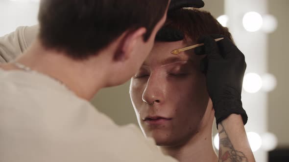 A Man Eyebrow Master Applying Wax on the Hairs of the Eyebrow of His Male Client