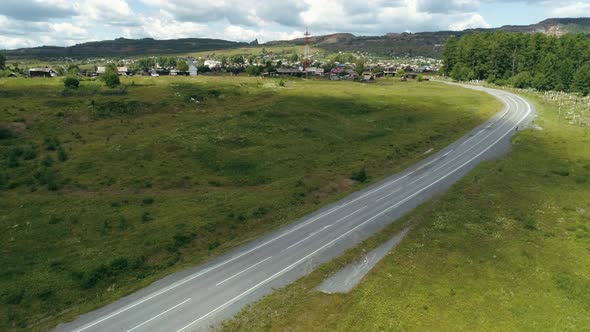 Aerial Countryside Road Running Through Green Fields Towards the Village