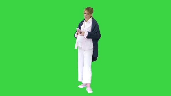 Pretty Pregnant Woman Using Her Smartphone Touching Her Belly Standing on a Green Screen, Chroma Key