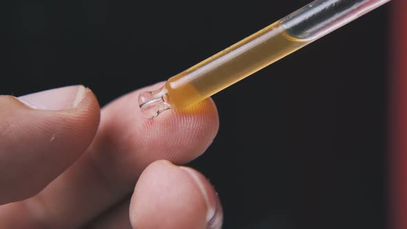 Man Holds Pipette with Brown Liquid on Black Background