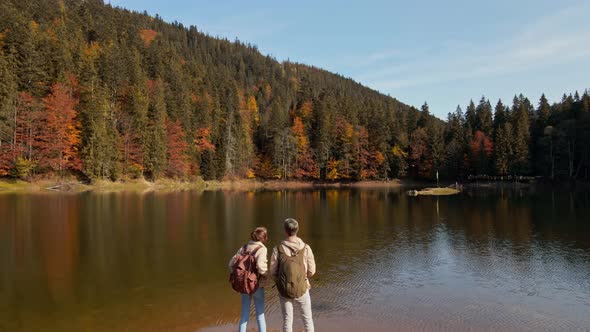 Aerial Slow Motion View of Couple Hikers Man and Woman on Shore of Beautiful Famous Mountain Lake