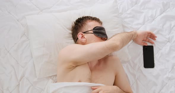 Sleeping Man Was Awakened By an Alarm Clock Guy Looks at the Phone Screen and Falls Asleep