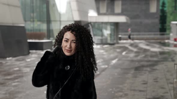 A Darkhaired Curlyhaired Woman Walks Through a Winter City Enjoying a Beautiful Day