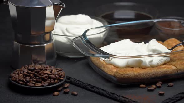 Savoiardi Ladyfingers Biscuits and Cream in Baking Dish, Coffe Maker on Dark Concrete Background