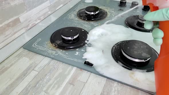 Woman in Protective Gloves Sprays on the Surface of the Gas Stove Cleaning Agent To Remove Fat