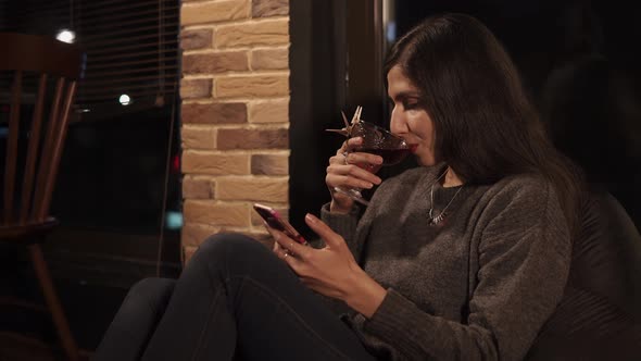 A Young Married Woman Sits on a Cushion Chair in a Cafe and Drinks a Cocktail