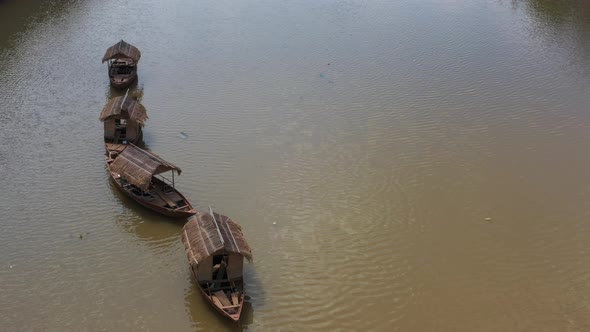 Aerial view of a line of four small traditional Asian fishing boats are tied up in a canal and movin