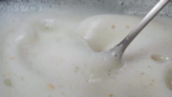 Stirring instant porridge with milk and oatmeal. A metal spoon mixes cereal and dairy