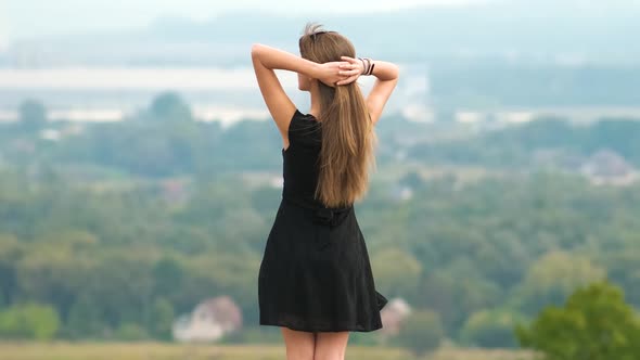 Young Pretty Woman with Long Hair in Black Short Dress Standing Outdoors Enjoying View of Summer